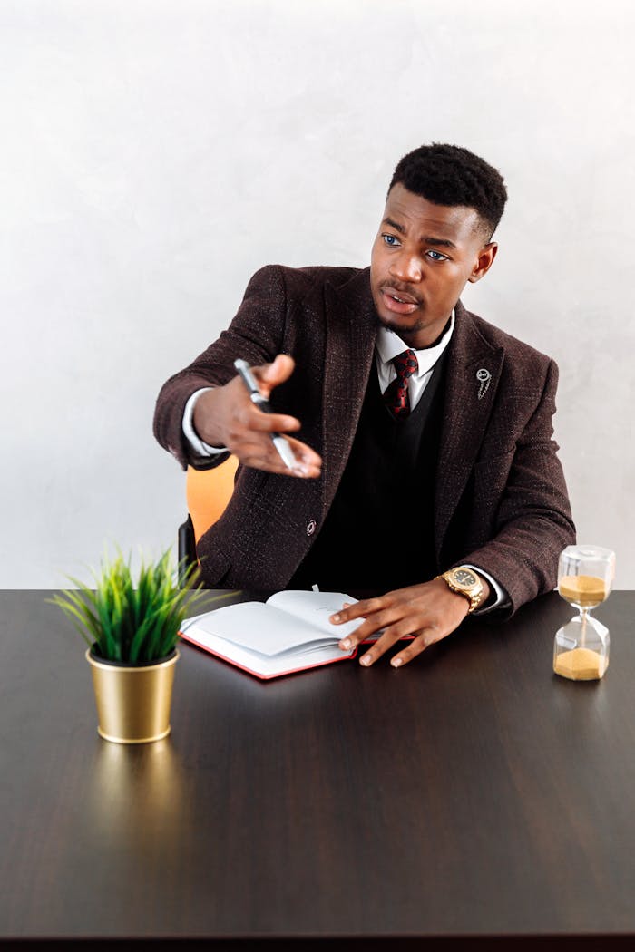 Confident businessman gesturing during an office meeting with a notebook and timer on the desk.