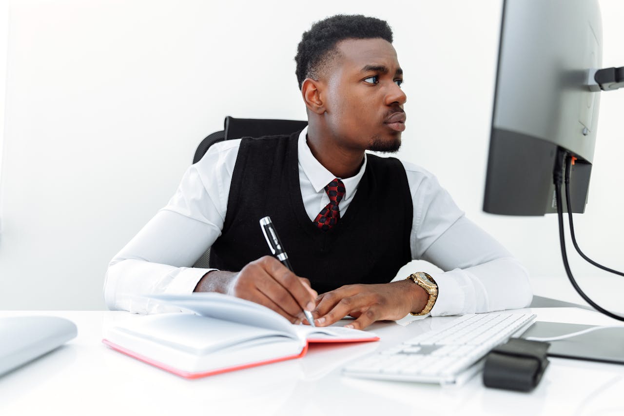 Professional businessman writing notes while working on a computer in a modern office.
